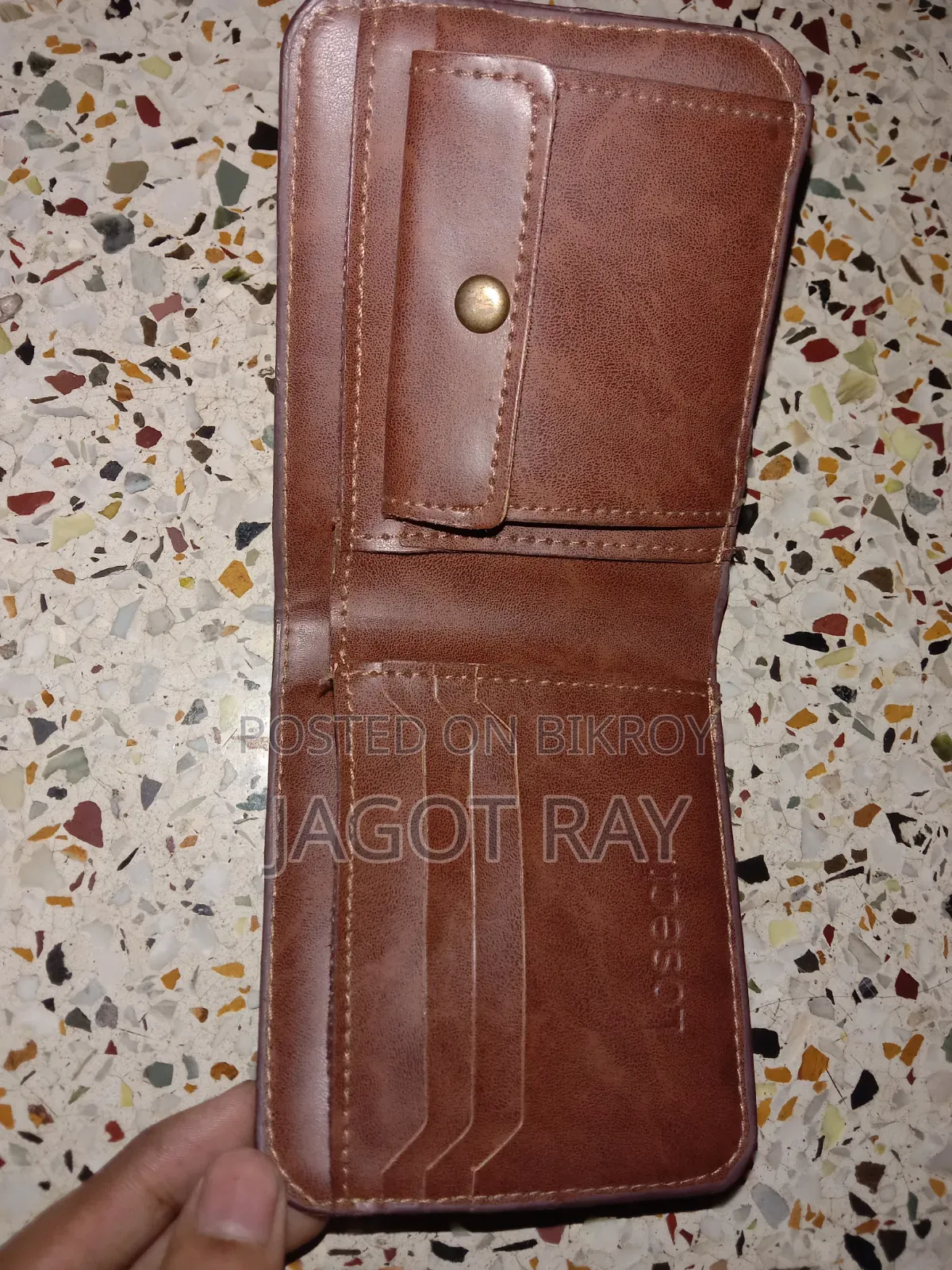 এটি বাদামী চামড়ার ওয়ালেট, যার কিনারায় সেলাইয়ের কাজ করা আছে।
